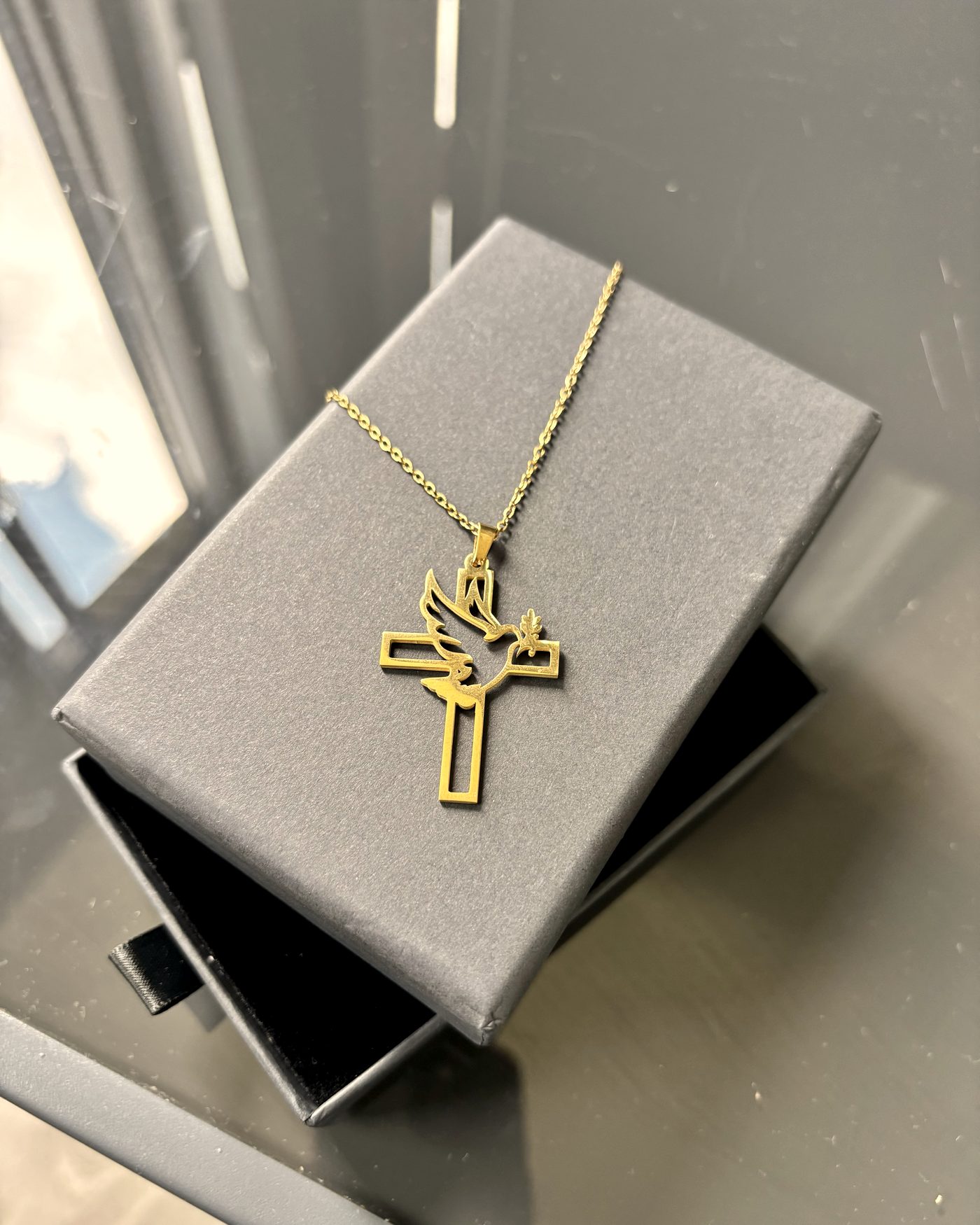 The dove-and-cross pendant in gold, resting on its gift box.